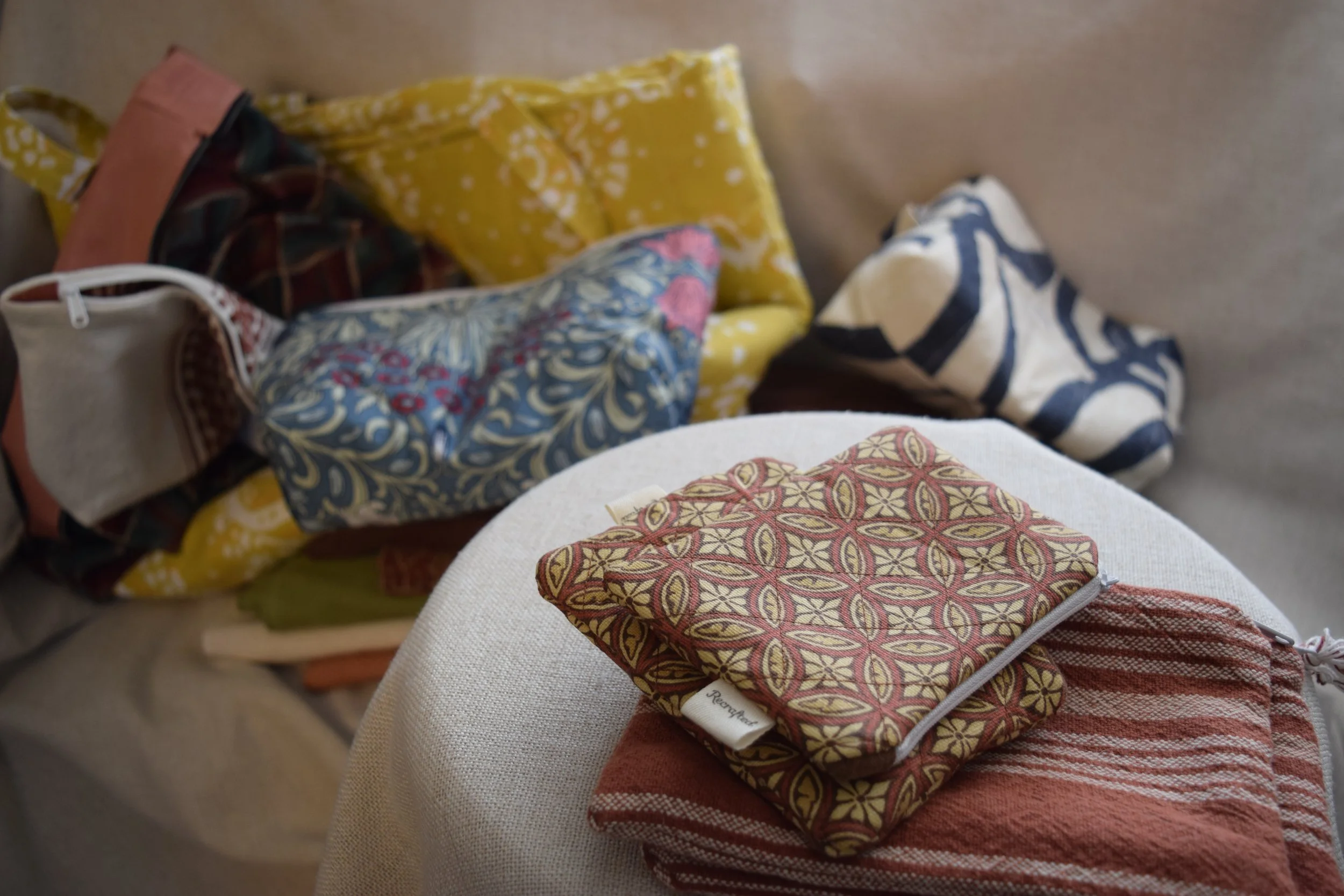 Various pieces of patterned fabric and cloth items placed on a covered surface, including a small, zippered pouch with a geometric design and a folded cloth with stripes.
