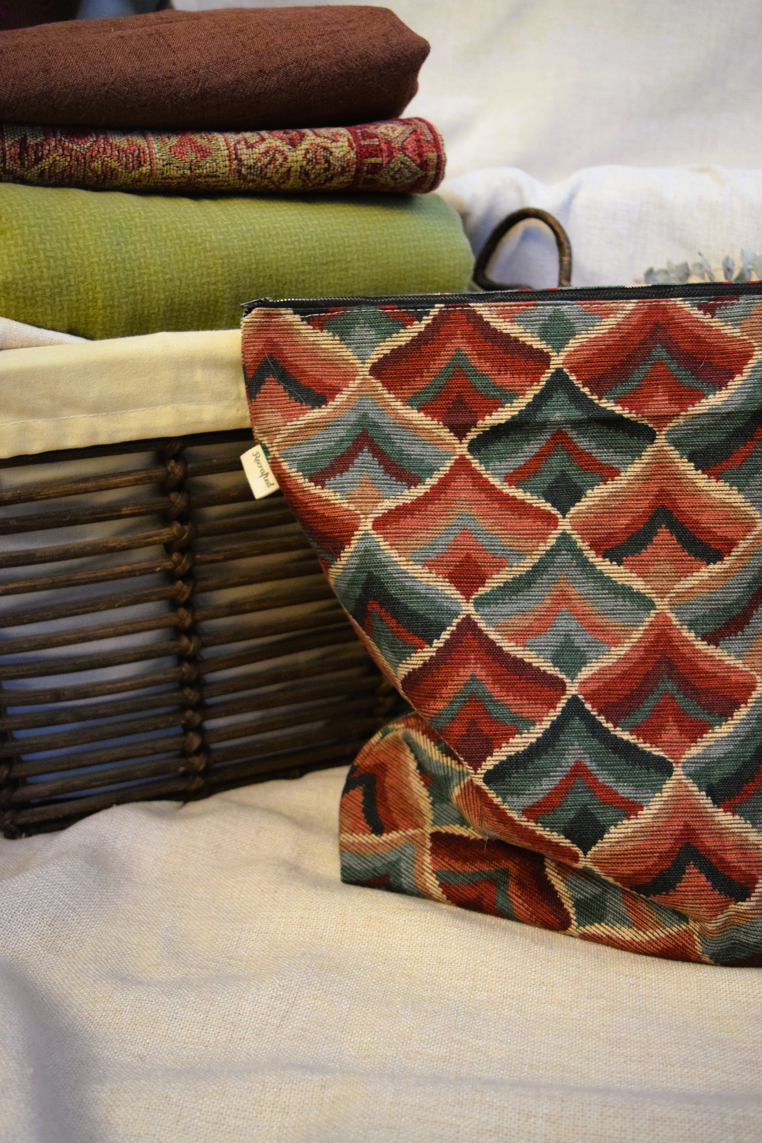 Stack of colorful folded rugs and pillows on a wicker basket with a decorative fabric bag in the foreground.