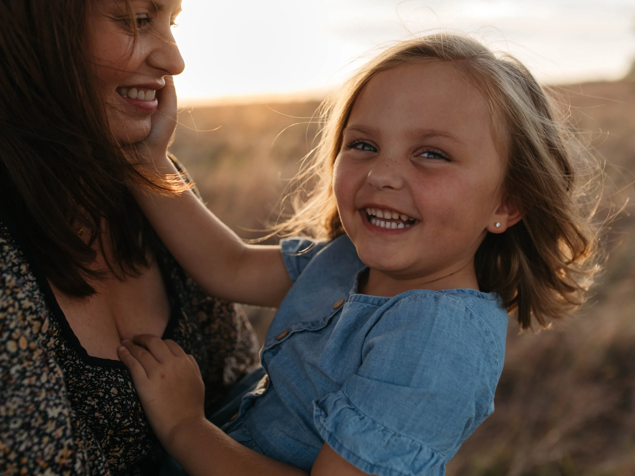 A woman and a young girl sharing a happy moment outdoors at sunset in Aledo Texas, smiling at each other.