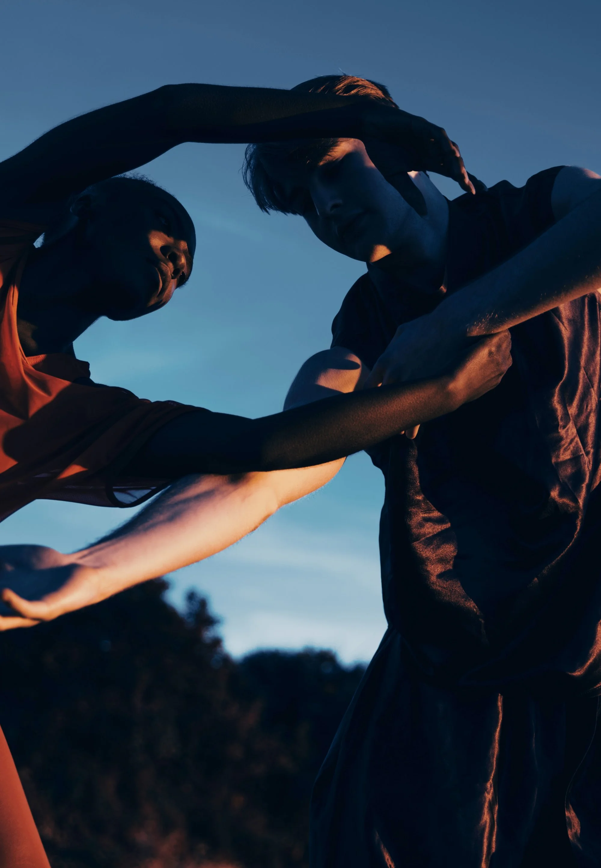 Two dancers reaching toward each other against a dusk sky