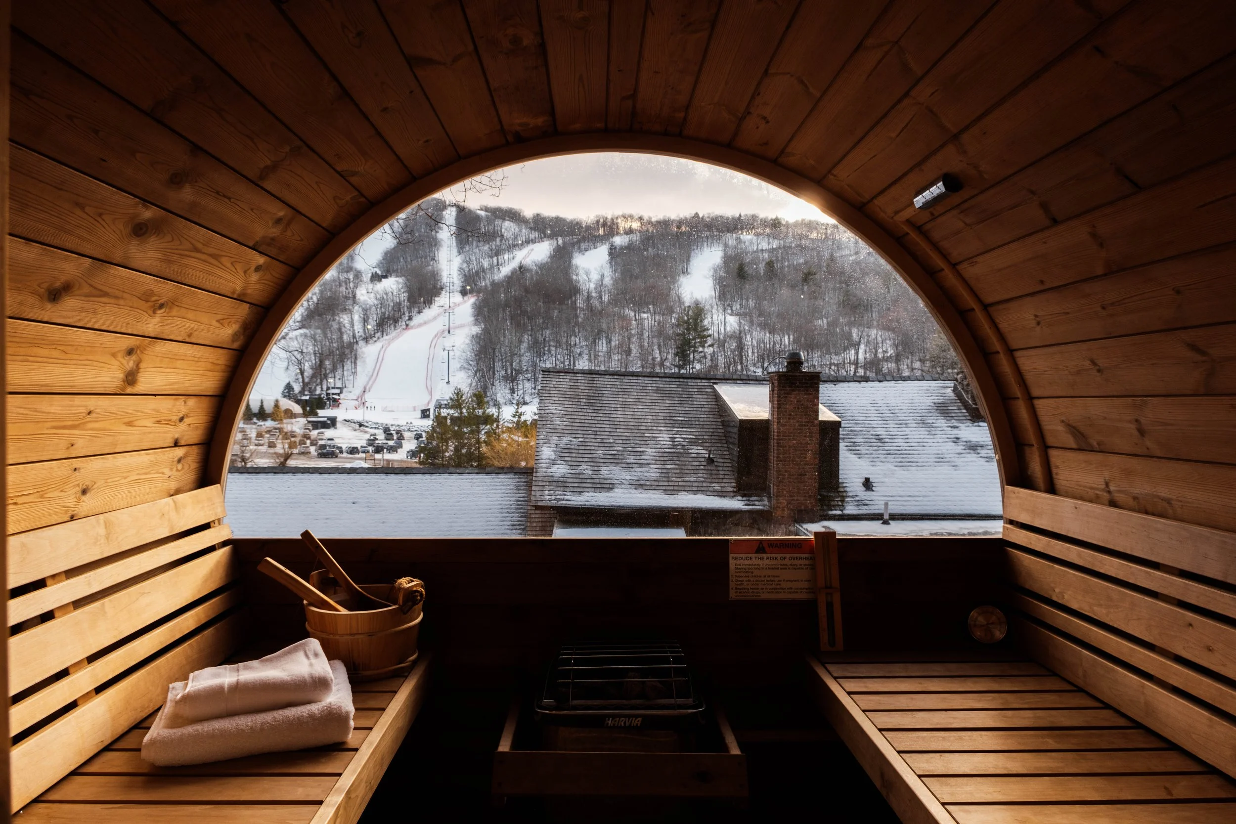 Inside a wooden sauna overlooking a snowy mountainous landscape with ski slopes and trees.