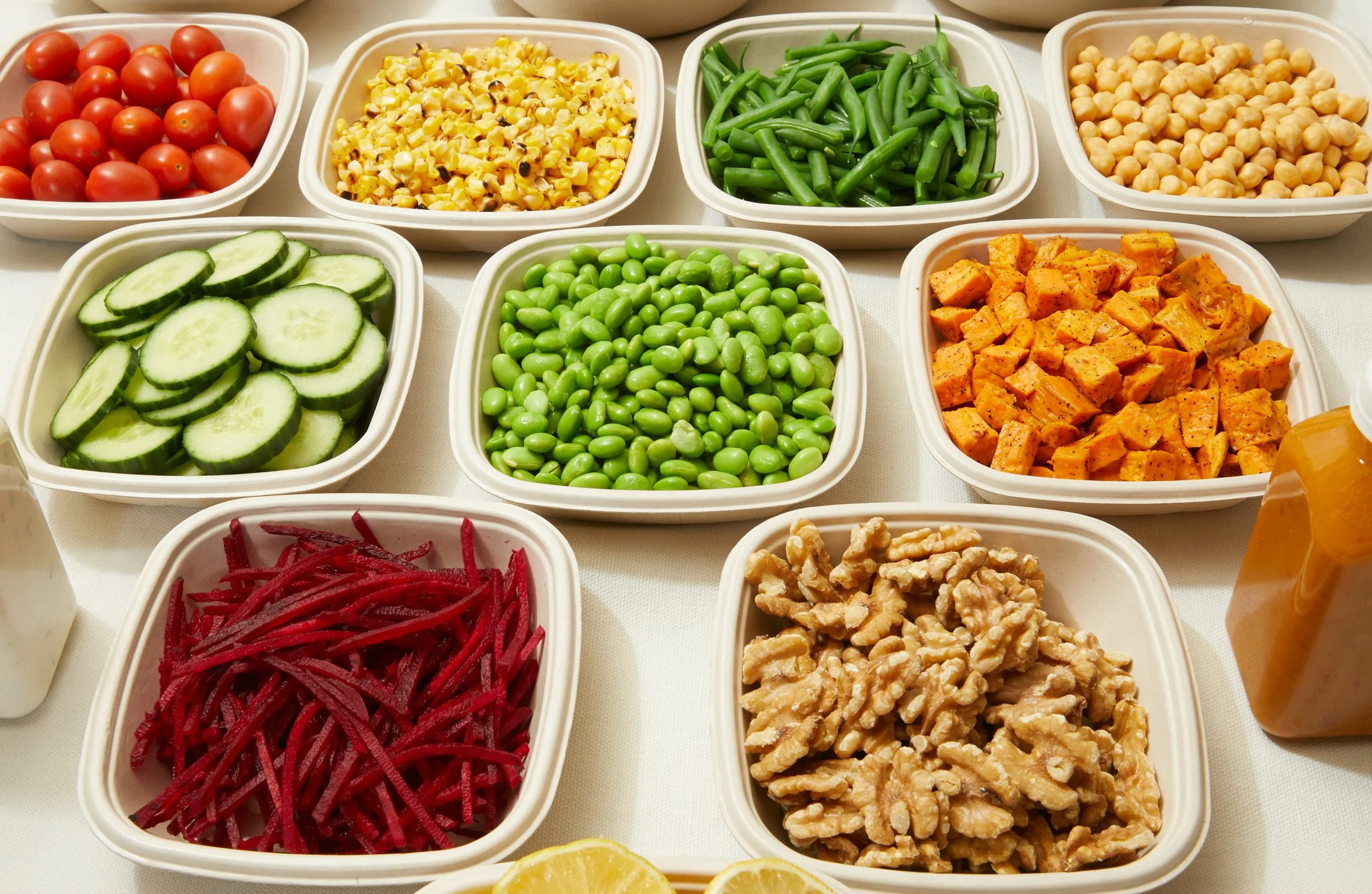 Assorted chopped vegetables including cherry tomatoes, corn, green beans, chickpeas, cucumbers, edamame, grilled chicken, shredded beets, walnuts, and honey mustard dressing.