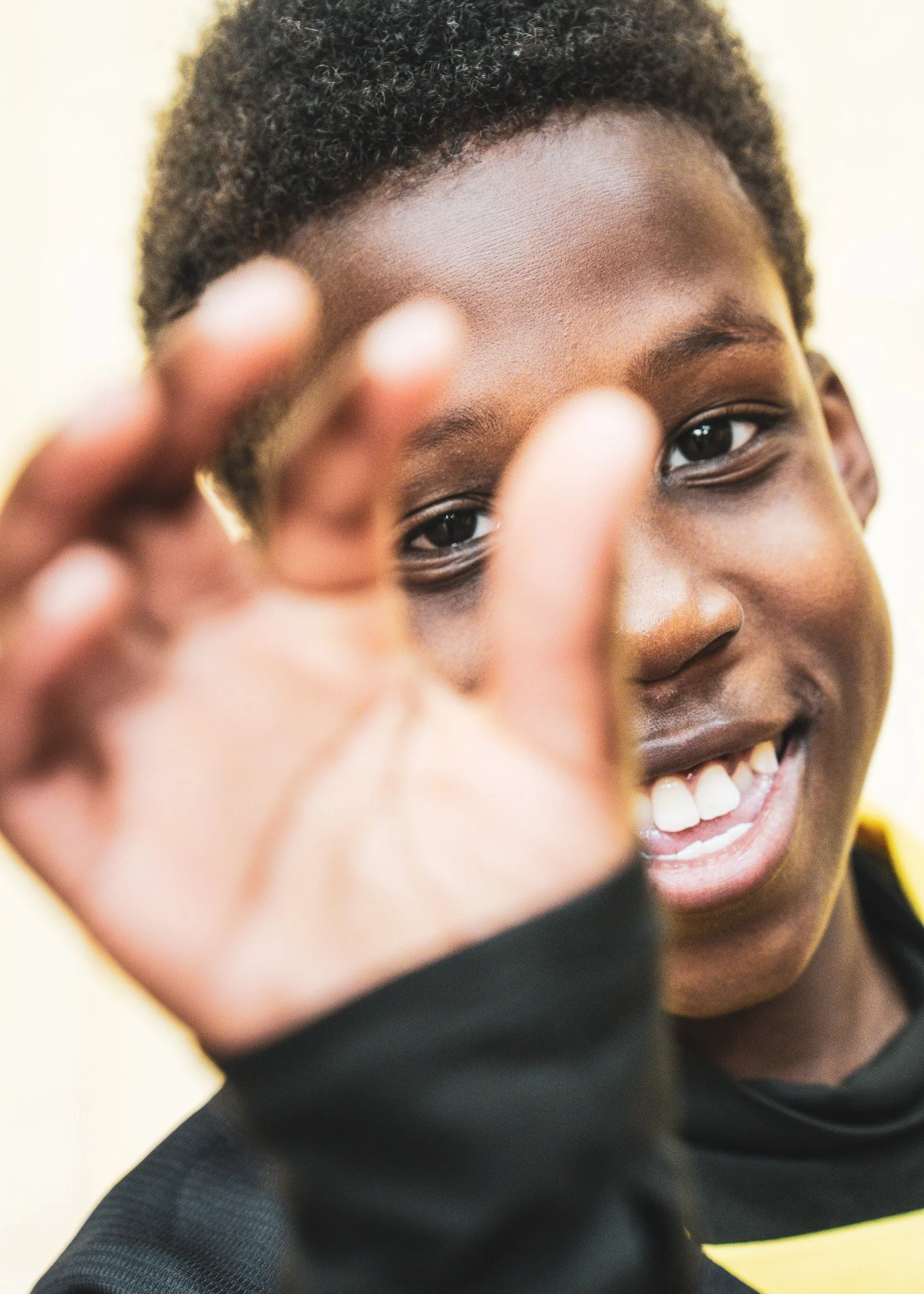Close-up of a person smiling and holding his hand close to the camera, with short curly hair and dark skin.