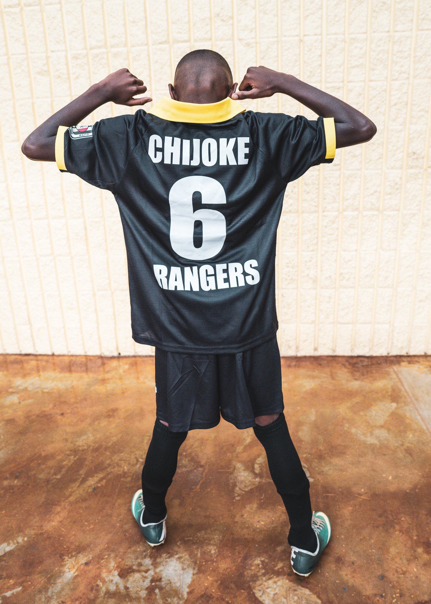 An athlete standing on a brown wooden sports court, facing away, wearing a black sports jersey with the name 'Chijoke', number 6, and 'Rangers' printed on the back, black shorts, and teal sneakers.