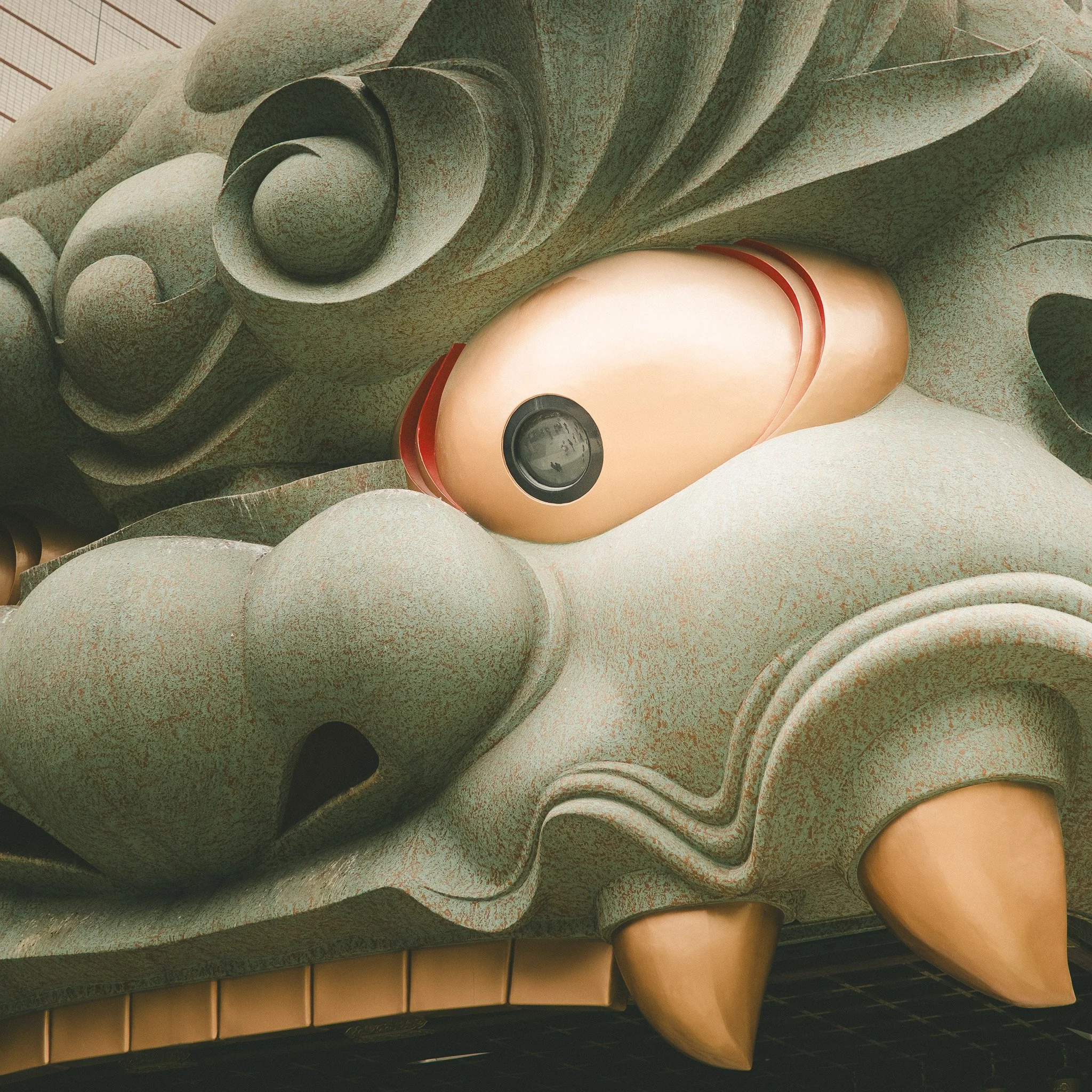 Close-up of a stone sculpture with flowing, abstract shapes and a smooth, rounded form at the bottom, resembling a stylized face or figure, with a background of tiled structure.