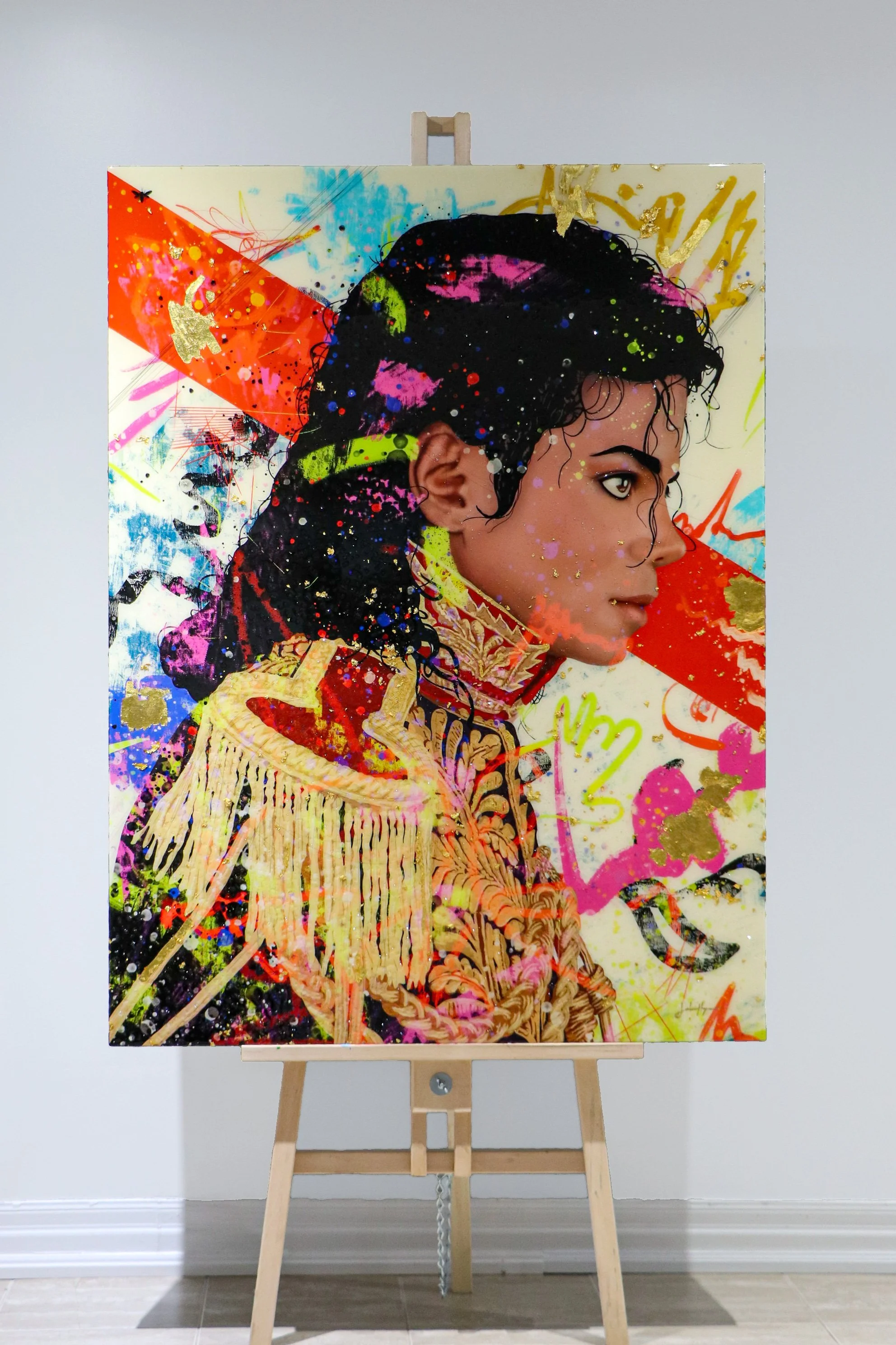 A colorful contemporary portrait painting on canvas of Michael Jackson in a military-style jacket with embroidered details, set on an easel against a plain white wall.