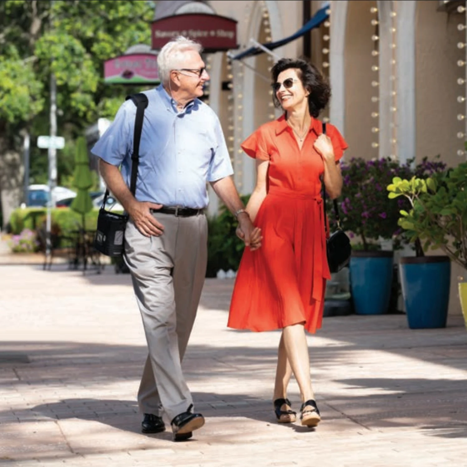 Active senior couple walking outdoors with Rhythm Healthcare P2-E6 Pulse Dose portable oxygen concentrator in carry bag - lightweight FAA-compliant travel design