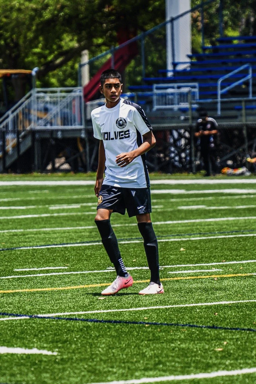 A young male soccer player standing on a green turf field during a game or practice session.