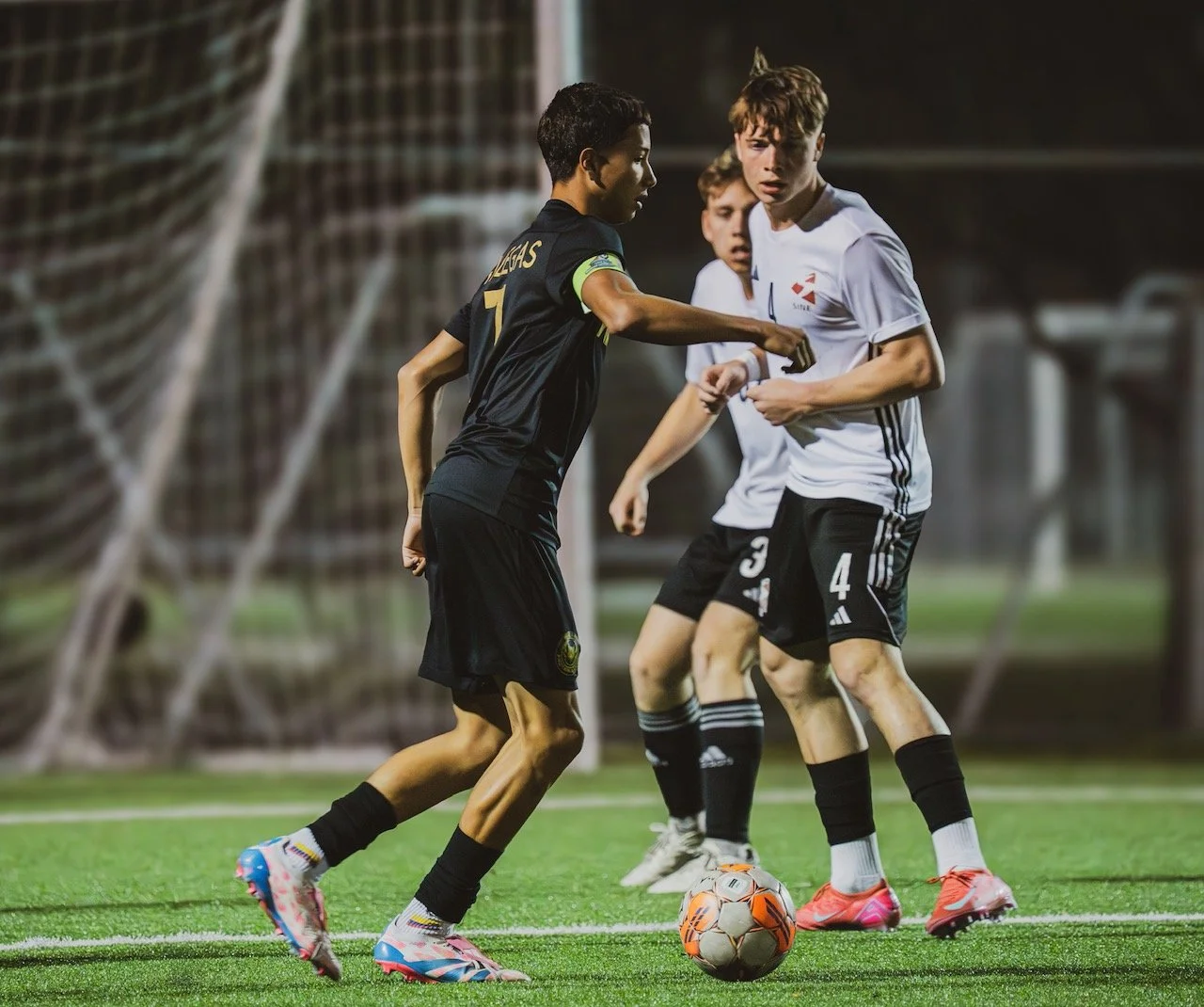 Young soccer players competing for the ball during a match on a field at night.