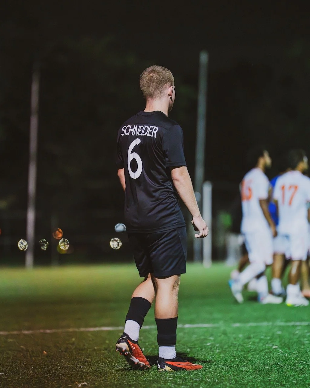 A soccer player wearing a black jersey with the name 'Schneider' and number 6 on the back, standing on a soccer field at night.