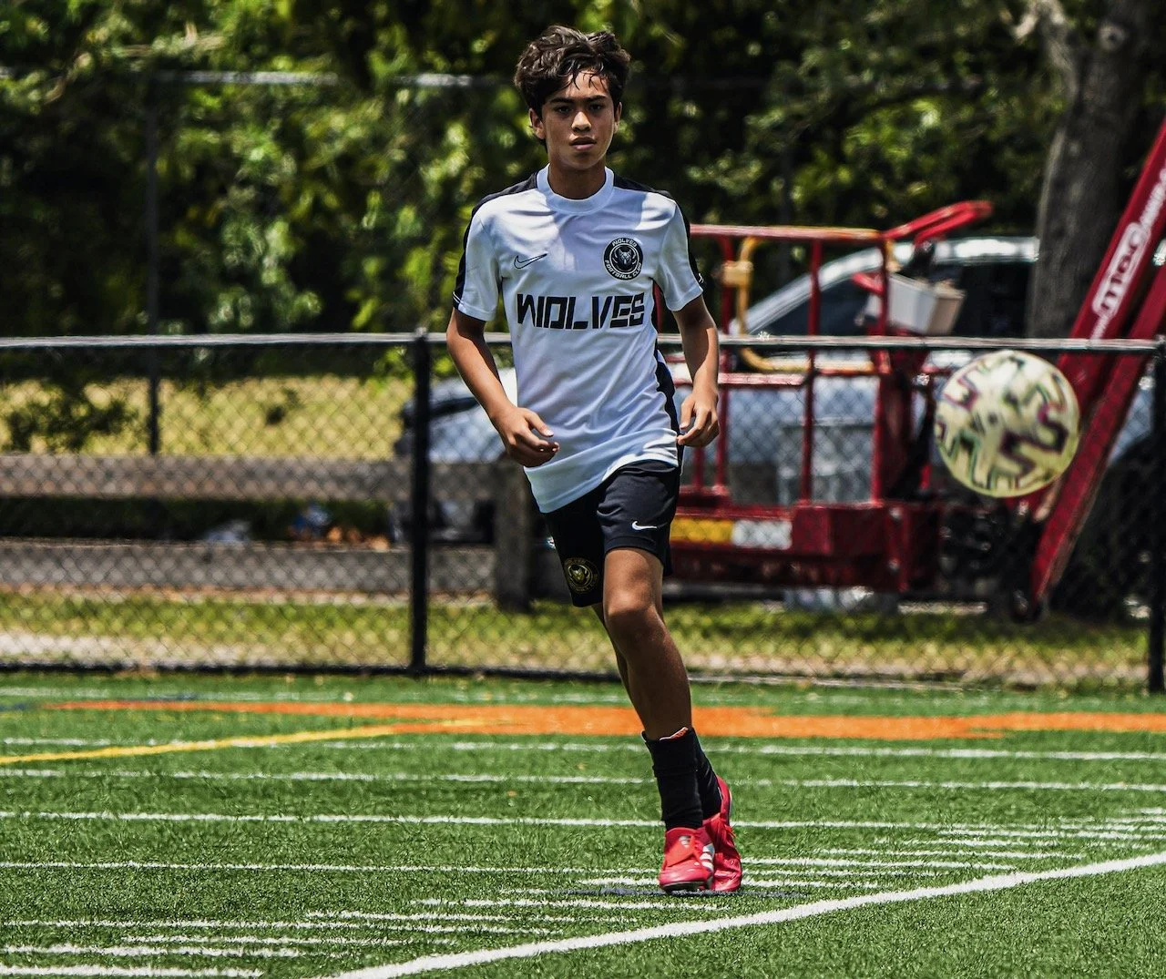 Young male soccer player running on a field with a white jersey and black shorts.