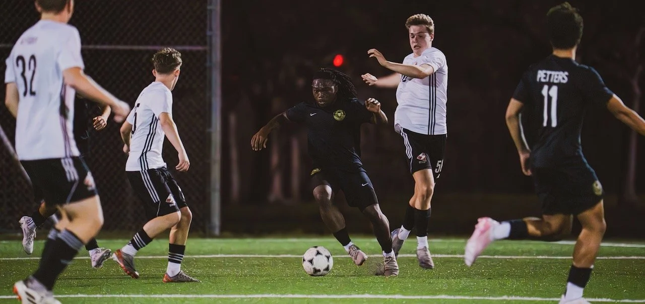 Soccer match with players in black and white jerseys competing for the ball on a field at night.