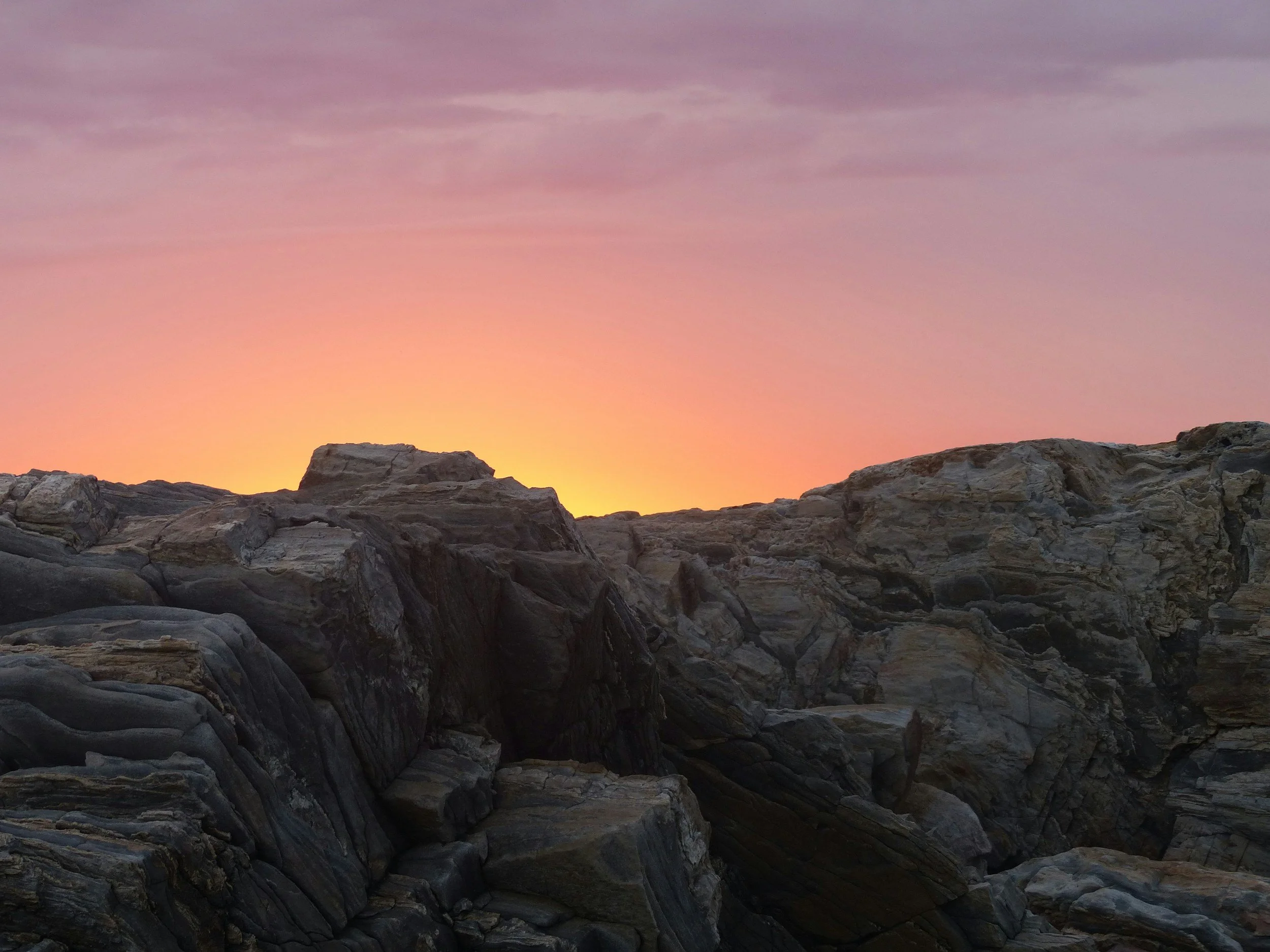 Rock formations at sunset with a colorful sky in pink, purple, and orange hues.