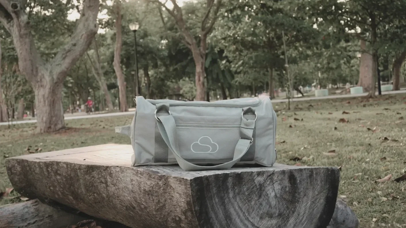 Grey Skylaris Duffel Bag (22L) resting on a rustic wooden log bench in a park. The versatile carry-on bag clearly displays the Skylaris logo and a quick-access front pocket, perfect for short trips and everyday essentials.