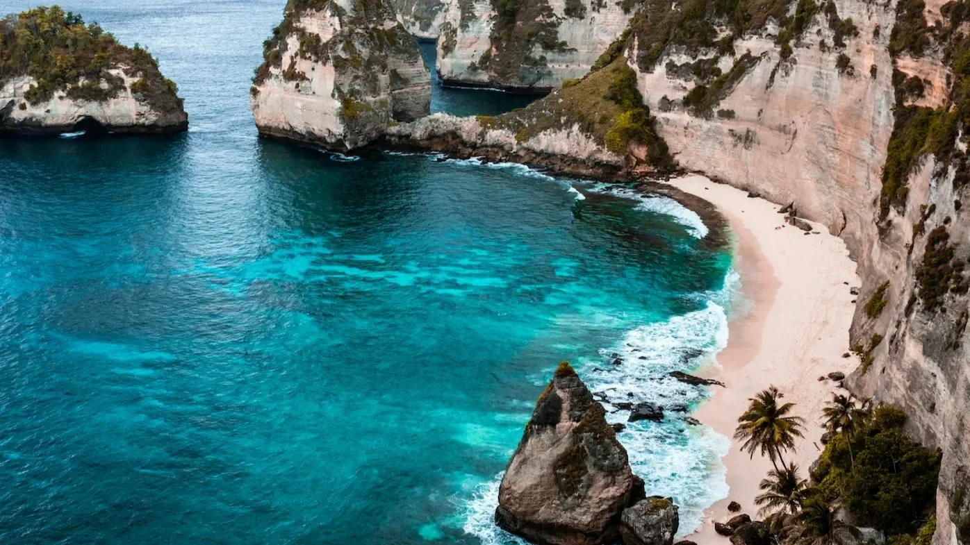 A picturesque Bali beach featuring clear blue water, white sand, and palm trees, evoking the feeling of a perfect tropical vacation and relaxation.