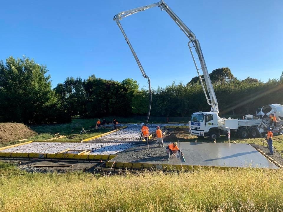 Construction workers are pouring concrete at a construction site during the daytime, with a cement truck pouring concrete into a foundation.