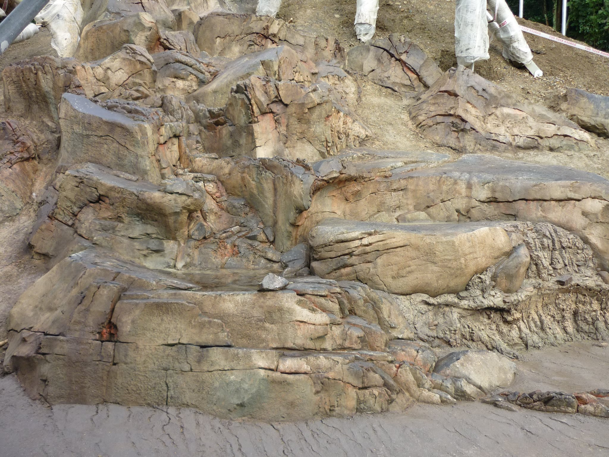 Rock formation with layers of sedimentary rock and a small amount of soil and grass at the top.