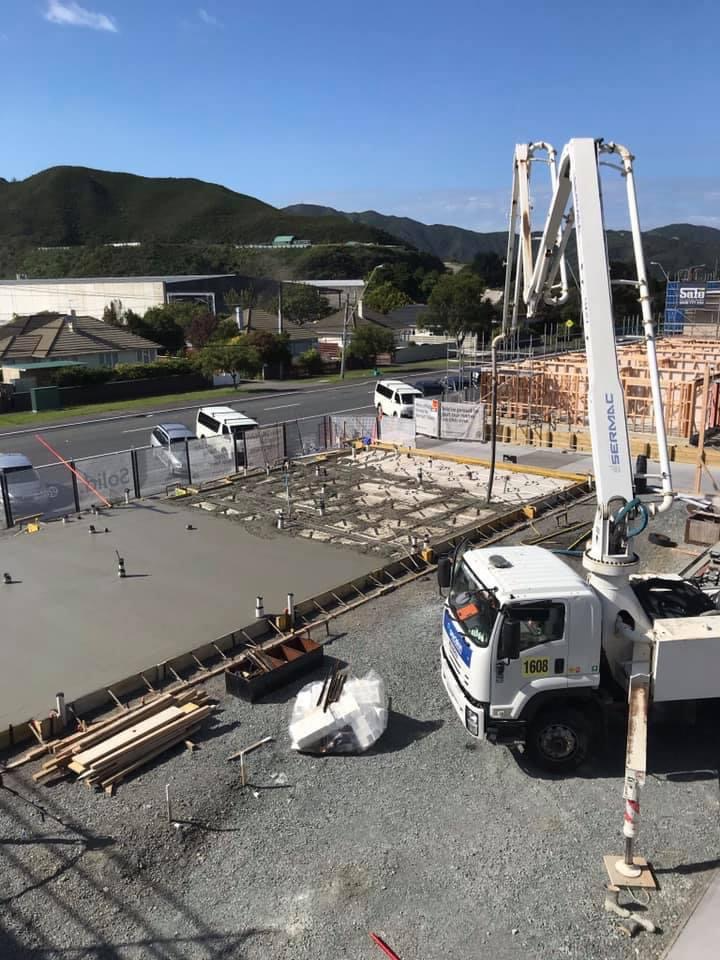 Construction site with a concrete slab, building frameworks, a crane truck, and construction tools, with a residential area and hills in the background.