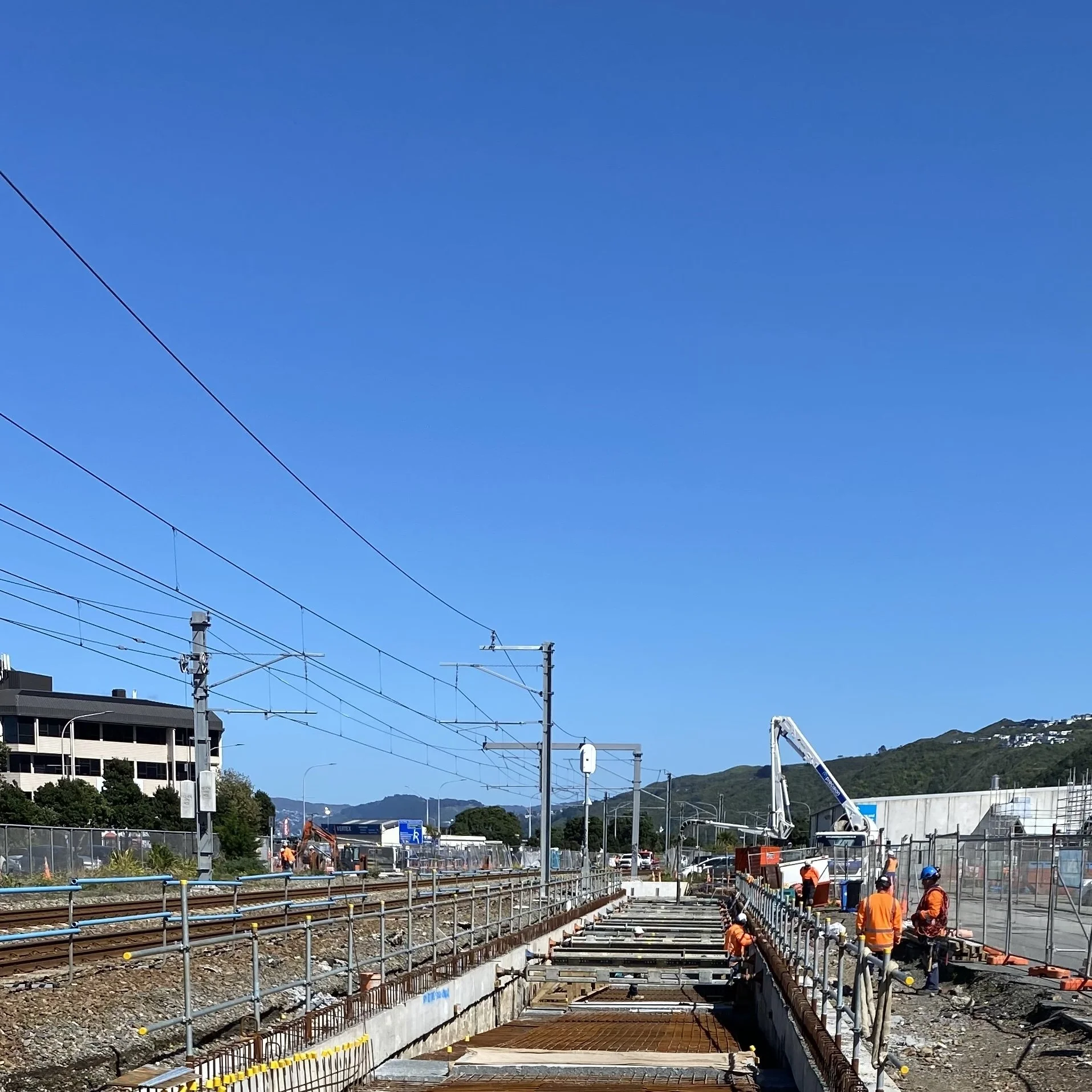 Precision Concrete Pumping and Spraying workers installing railway infrastructure, construction site, blue sky, hill in the background.
