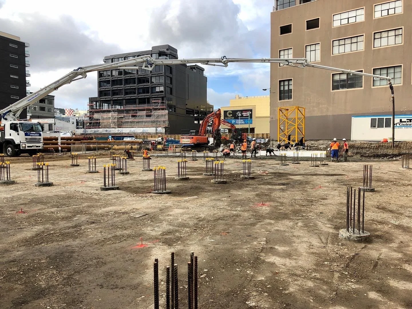 A Wellington construction site with Precision Concrete Pumping and Spraying  and equipment preparing building foundation in an urban area with tall buildings.