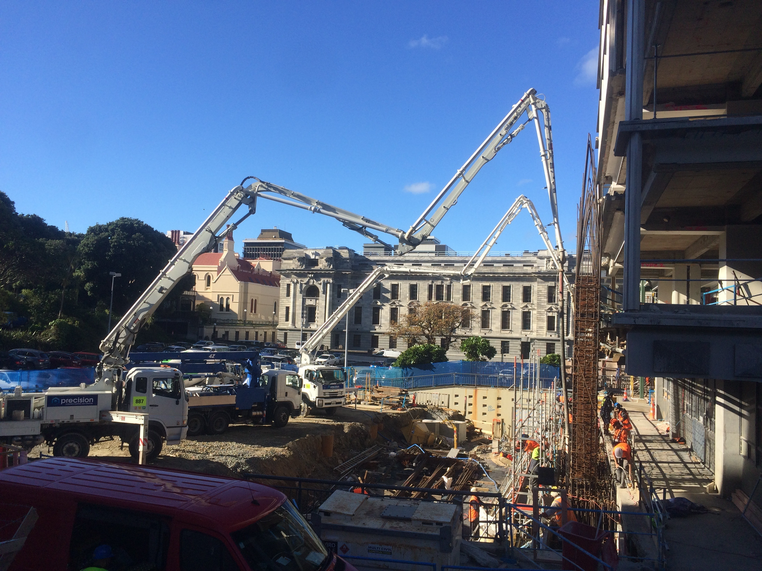 Construction site with trucks, workers, and scaffolding under a blue sky with some clouds.