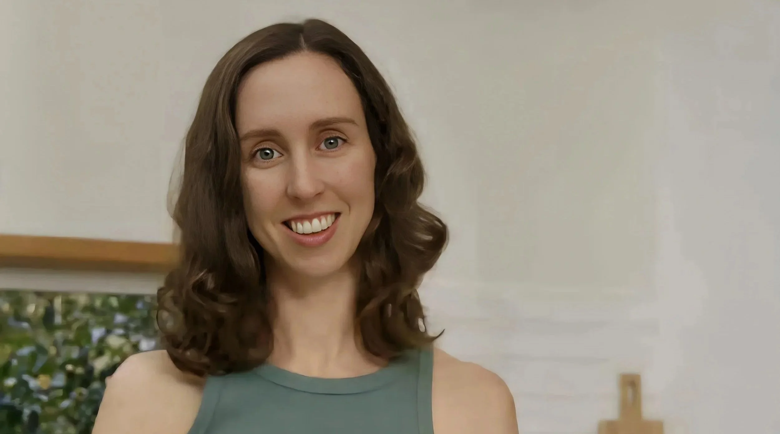 A woman with shoulder-length brown hair and blue eyes smiling indoors, wearing a sleeveless teal top.