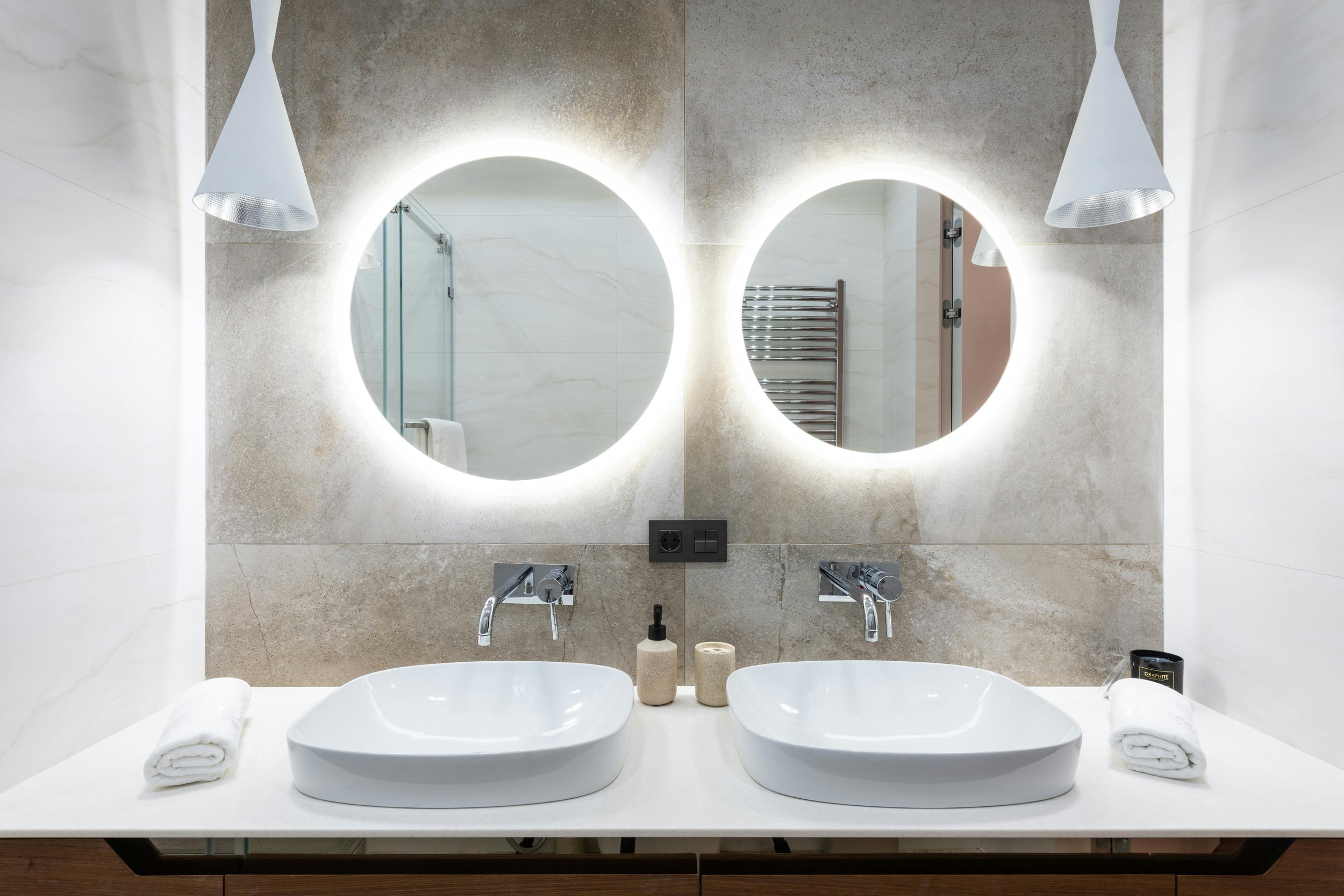 Modern bathroom with double sinks, illuminated round mirrors, and contemporary decor.