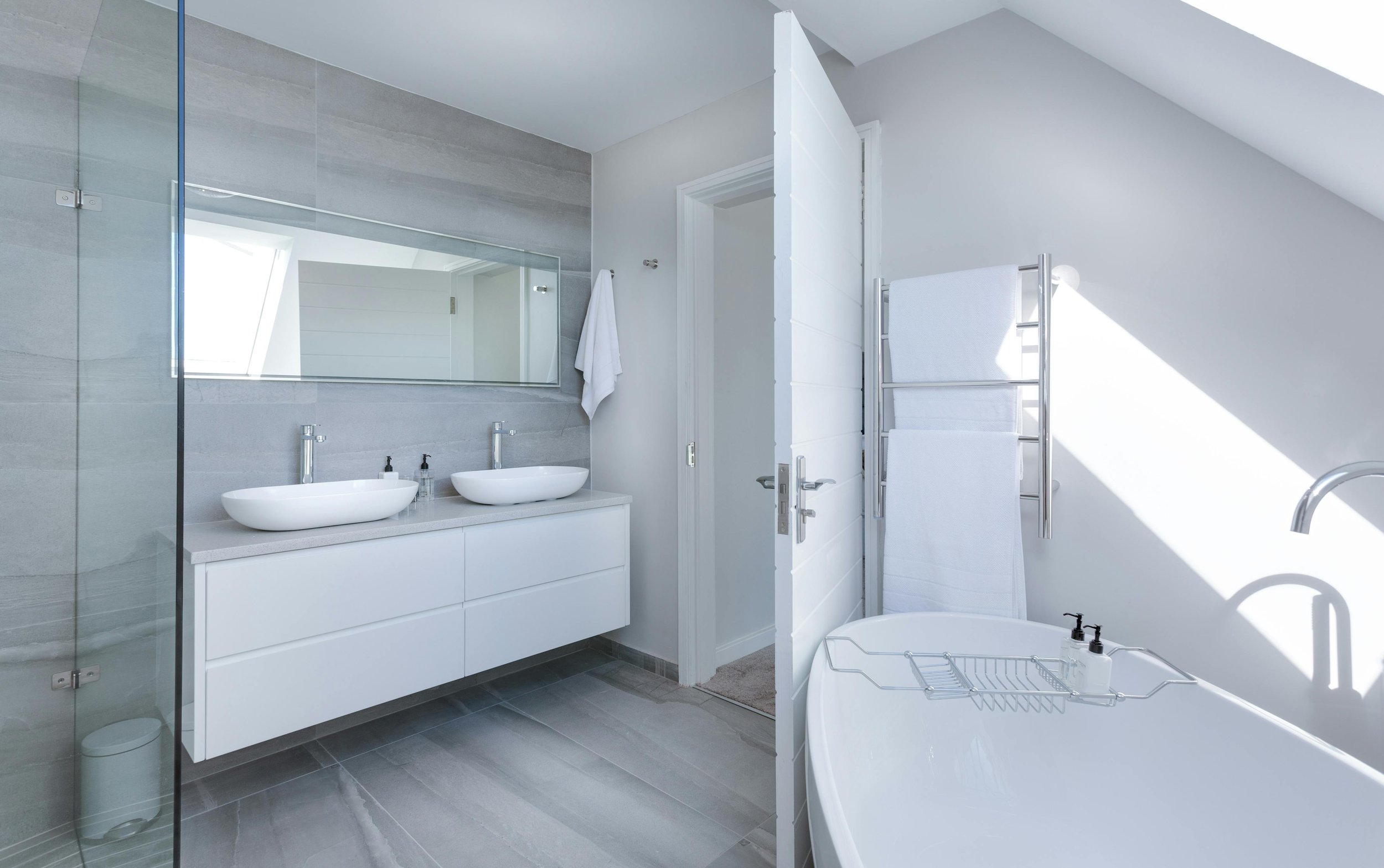 Modern bathroom featuring a double sink vanity, large wall mirror, walk-in shower, white bathtub, towel rack with white towels, and bright natural lighting.