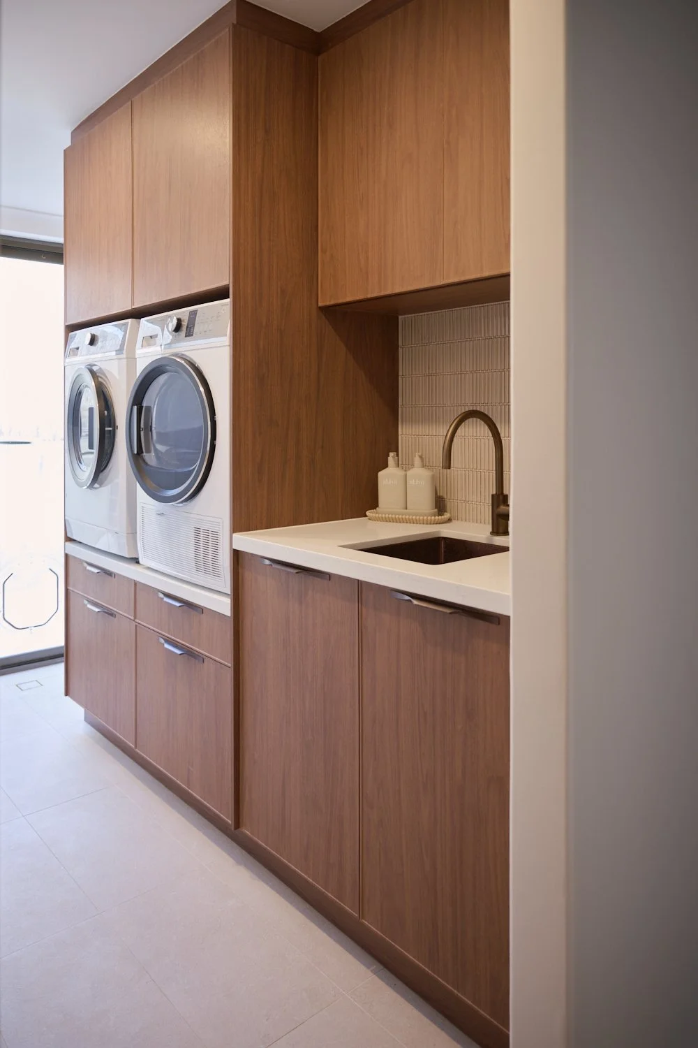Laundry room with wooden cabinets, a white washer and dryer, a small sink, and soap dispensers.