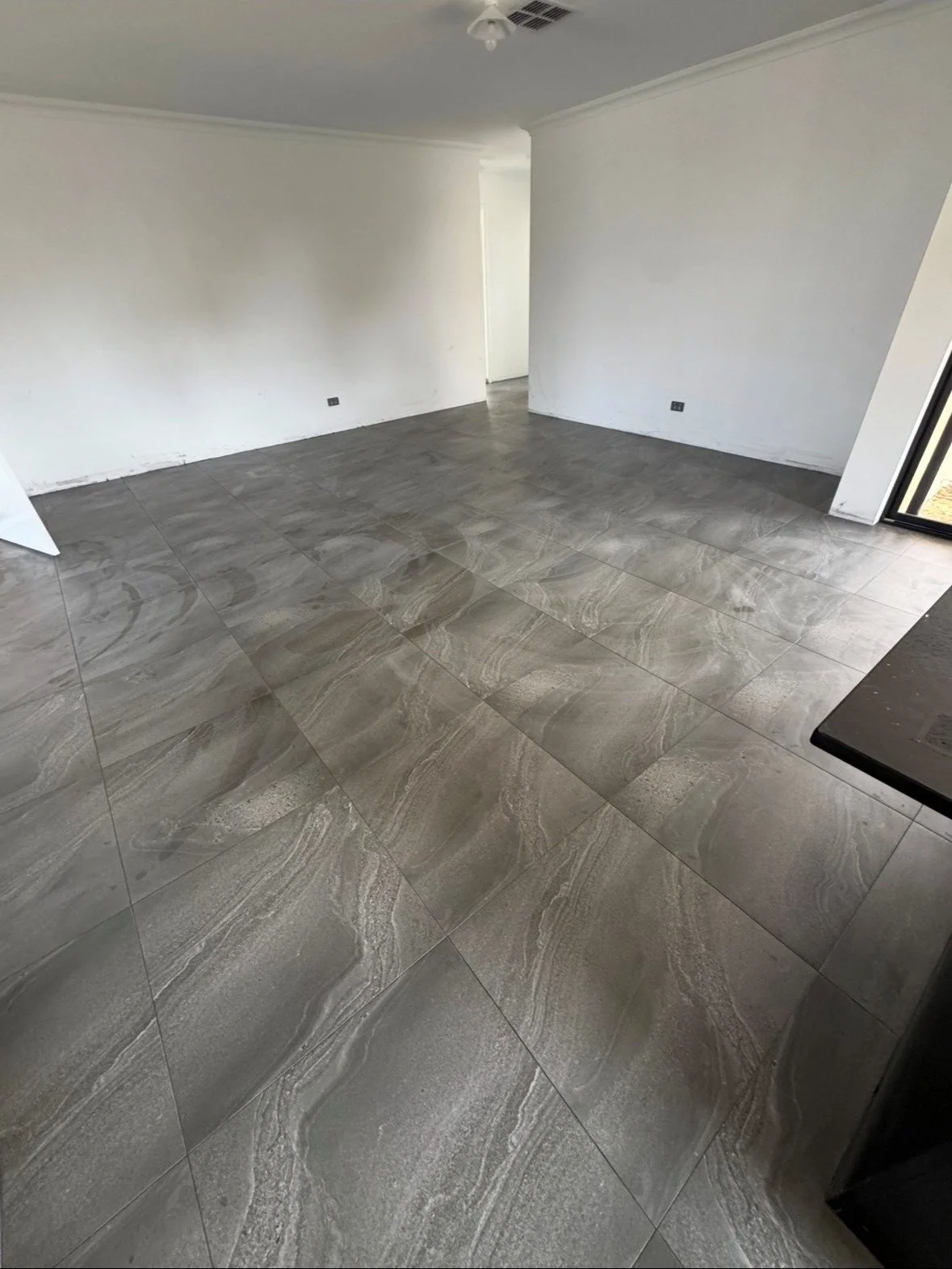 Empty room with gray tiled floor, white walls, and a sliding glass door leading outside.