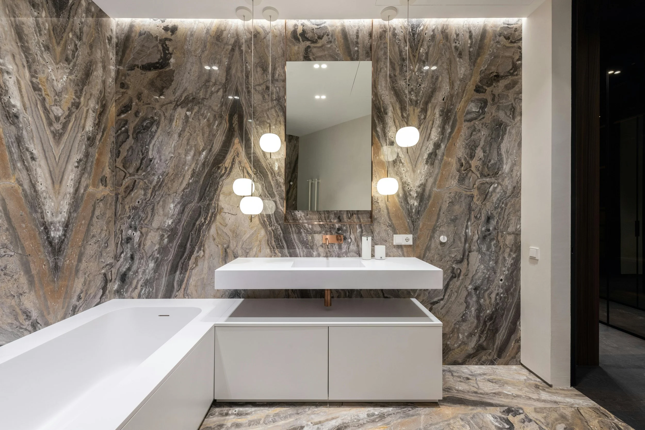 Modern bathroom with marble wall and floor, white vanity with a rectangular sink, large mirror, and hanging spherical pendant lights.