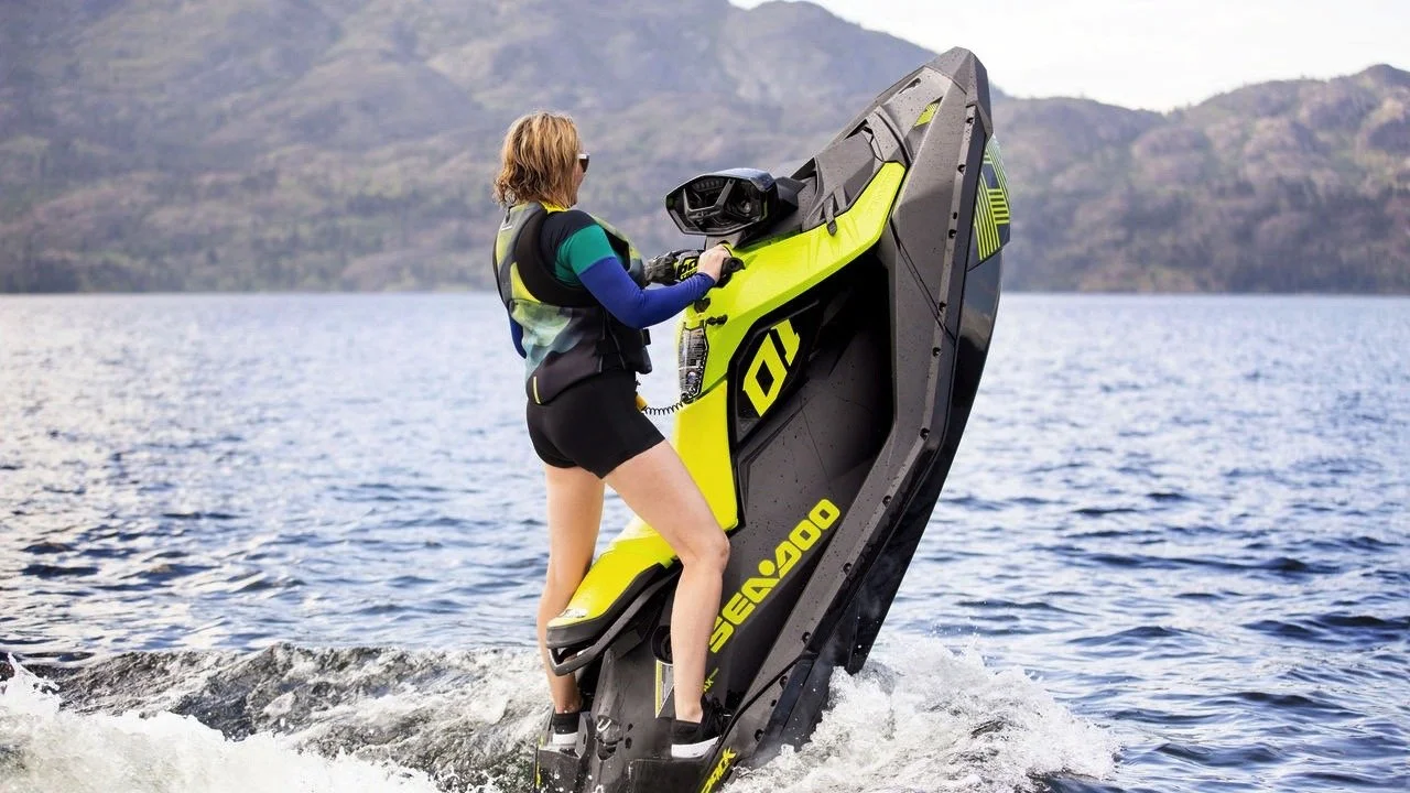Person som kjører en Sea-Doo vannscooter på vann, med fjell i bakgrunnen.