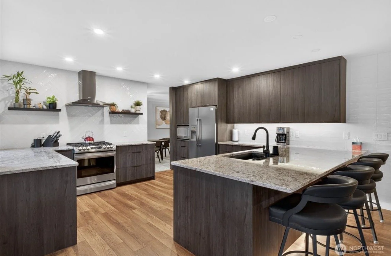 Modern kitchen with dark wood cabinets, granite countertops, stainless steel appliances, and a breakfast bar with black barstools.