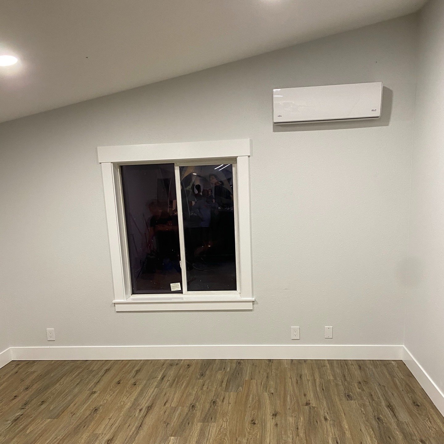 Empty room with white walls, a window, and a mounted air conditioning unit.