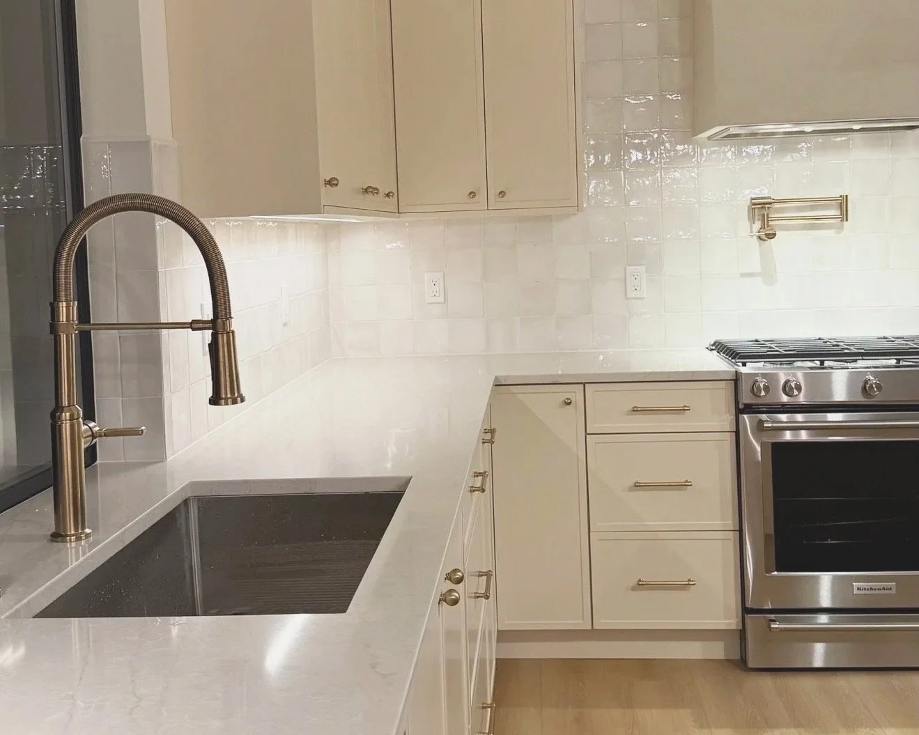 Modern kitchen with cream cabinetry, white marble countertop, stainless steel sink with a gooseneck faucet, and a stainless steel stove and oven.