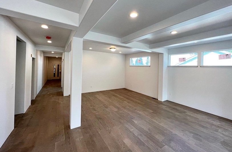 Empty room with white walls, wooden floors, and multiple ceiling lights, with windows along one wall.
