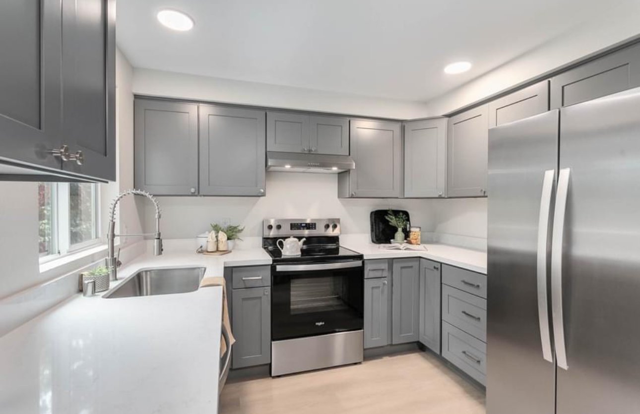 Modern kitchen with gray cabinets, stainless steel refrigerator, oven, and sink with window, decorated with small plants and kitchen accessories.