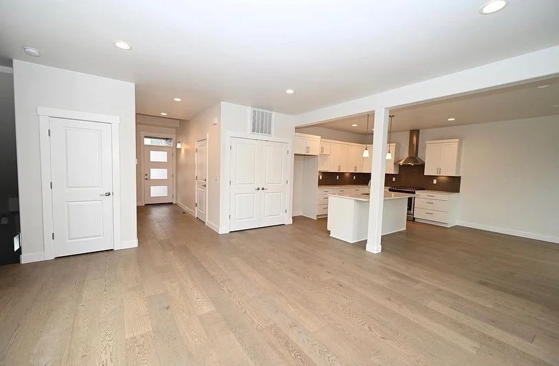Empty open-concept living space with white walls, white kitchen cabinets, a kitchen island, and wood flooring.