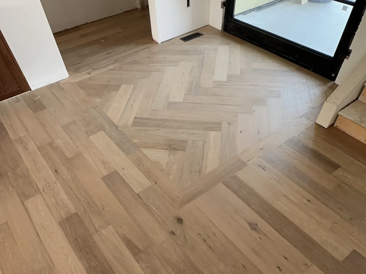 Wood flooring with a herringbone pattern near a glass door.
