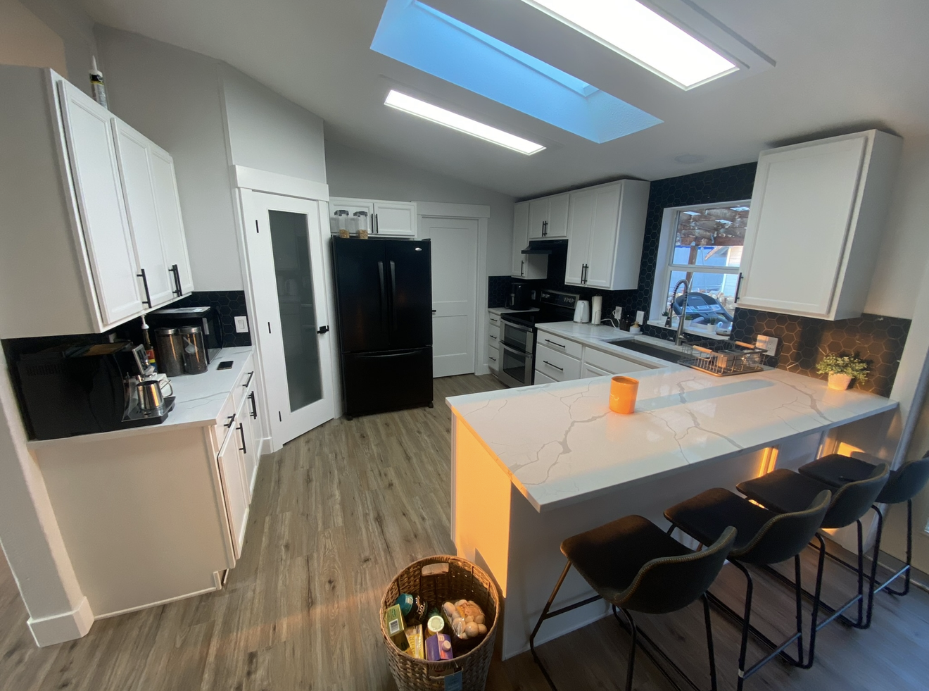A modern kitchen with white cabinets, black appliances, a marble island with orange underlighting, and three black barstools.