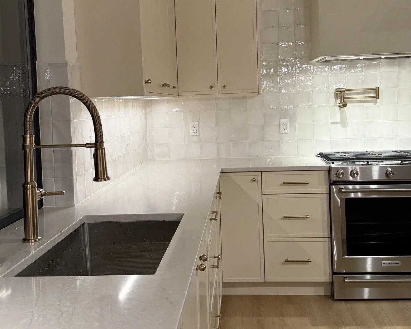 Modern kitchen with marble countertop, beige cabinets, stainless steel stove, and black sink with a gold faucet.