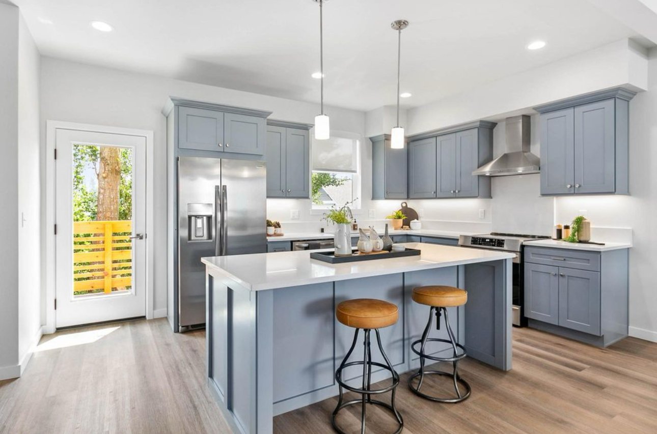 Modern kitchen with light blue cabinets, white countertops, stainless steel refrigerator, and island with two brown stools.