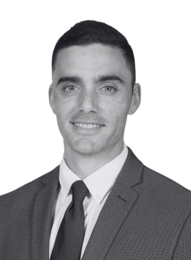 Black and white professional headshot of a young man in a suit and tie, smiling at the camera.