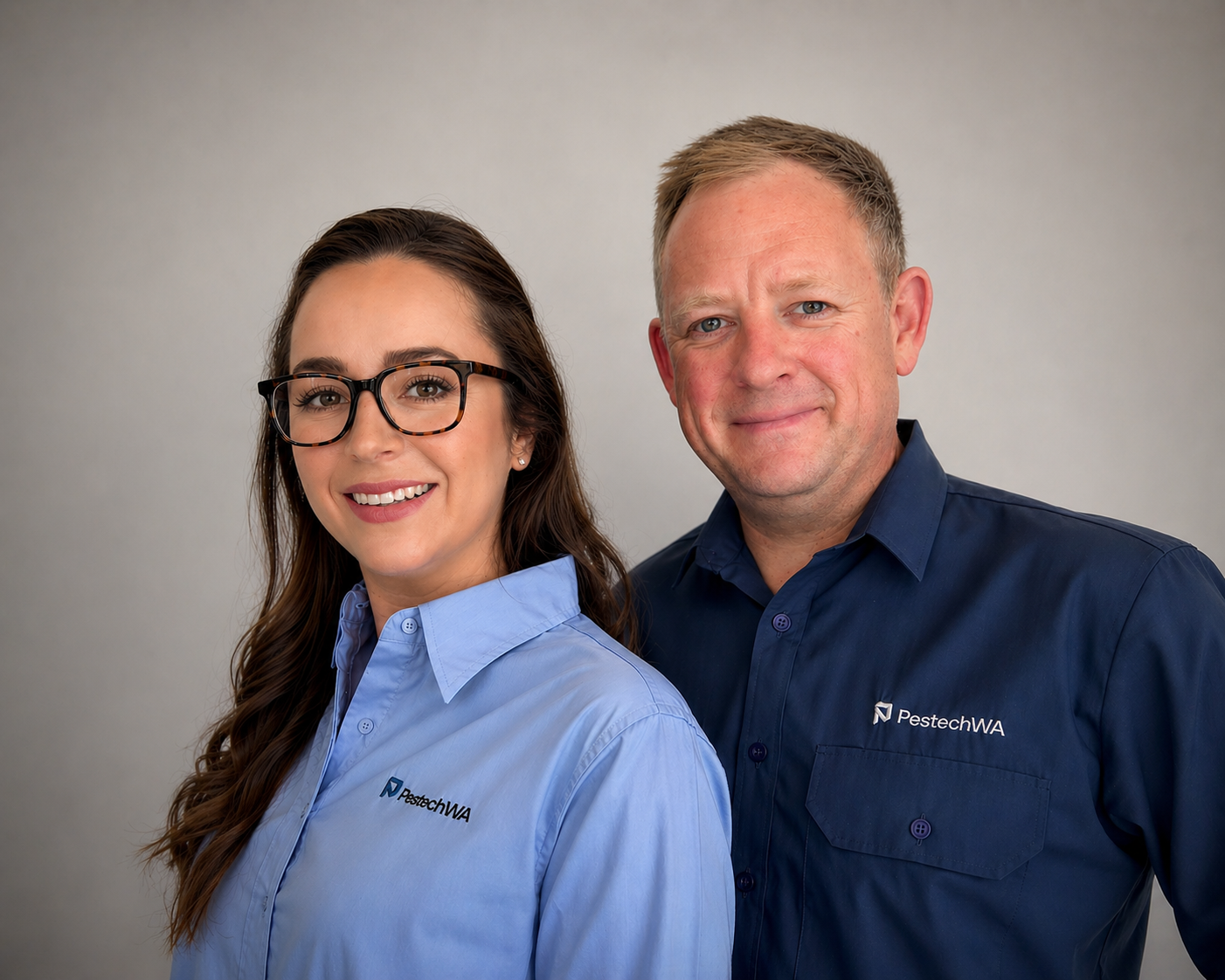 A woman and a man posing for a photo, both wearing blue shirts with the PestechWA logo. The woman is wearing glasses and has long brown hair, and the man has short blond hair.