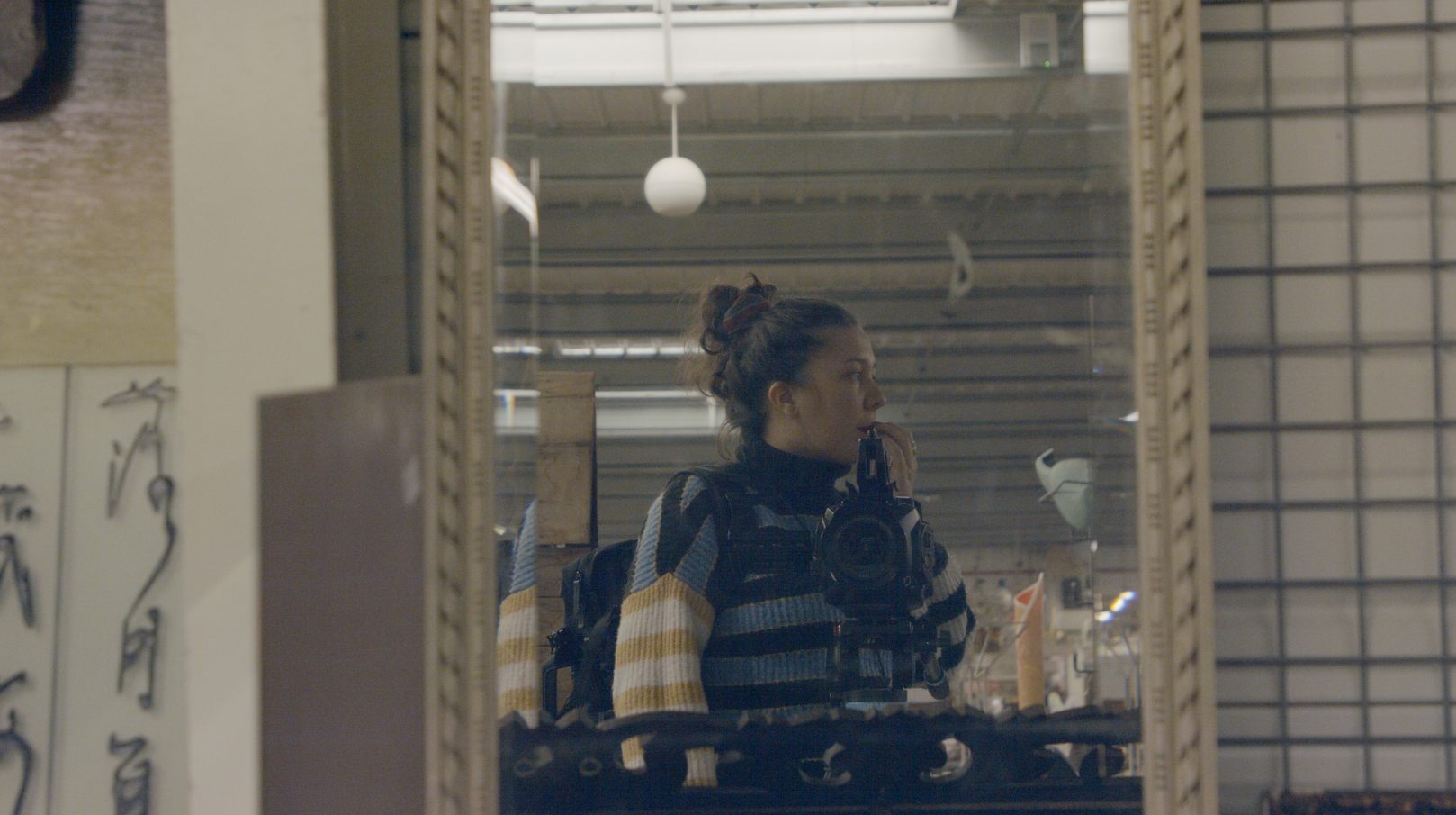Jeune femme prenant une photo dans un miroir, portant un pull rayé jaune, noir et blanc, avec un sac à dos