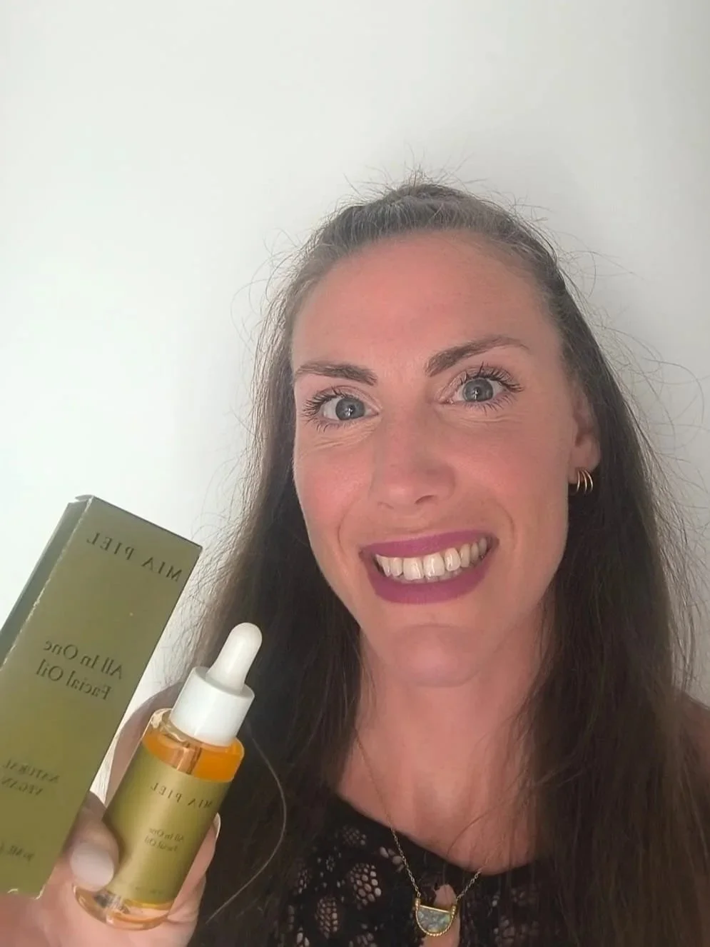 Smiling woman holding a green skincare product box and amber dropper bottle labeled Wild Wild Oil.