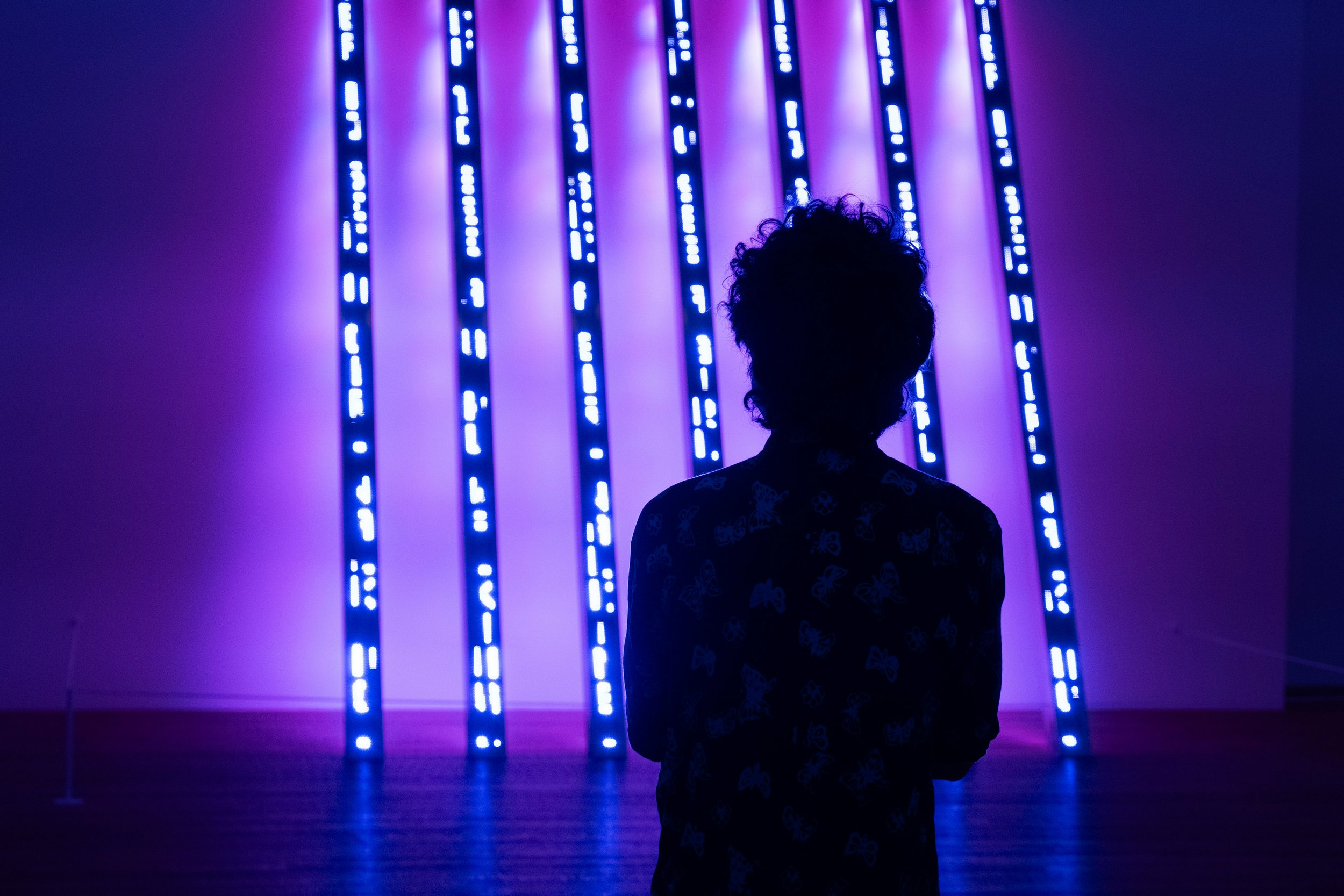 Silhouette eines Kindes vor einer Wand mit blauen Neonlichtern in einem dunklen Raum.