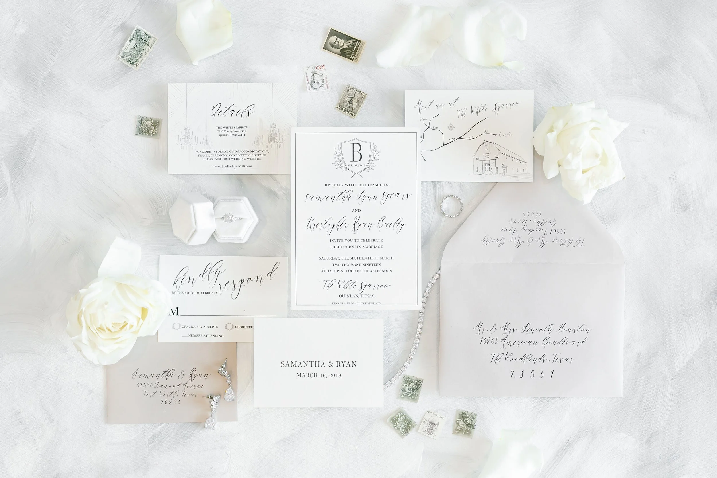 Wedding invitation suite and stationery with floral accents, jewelry, and postage stamps on a white textured surface in Atlanta, GA.