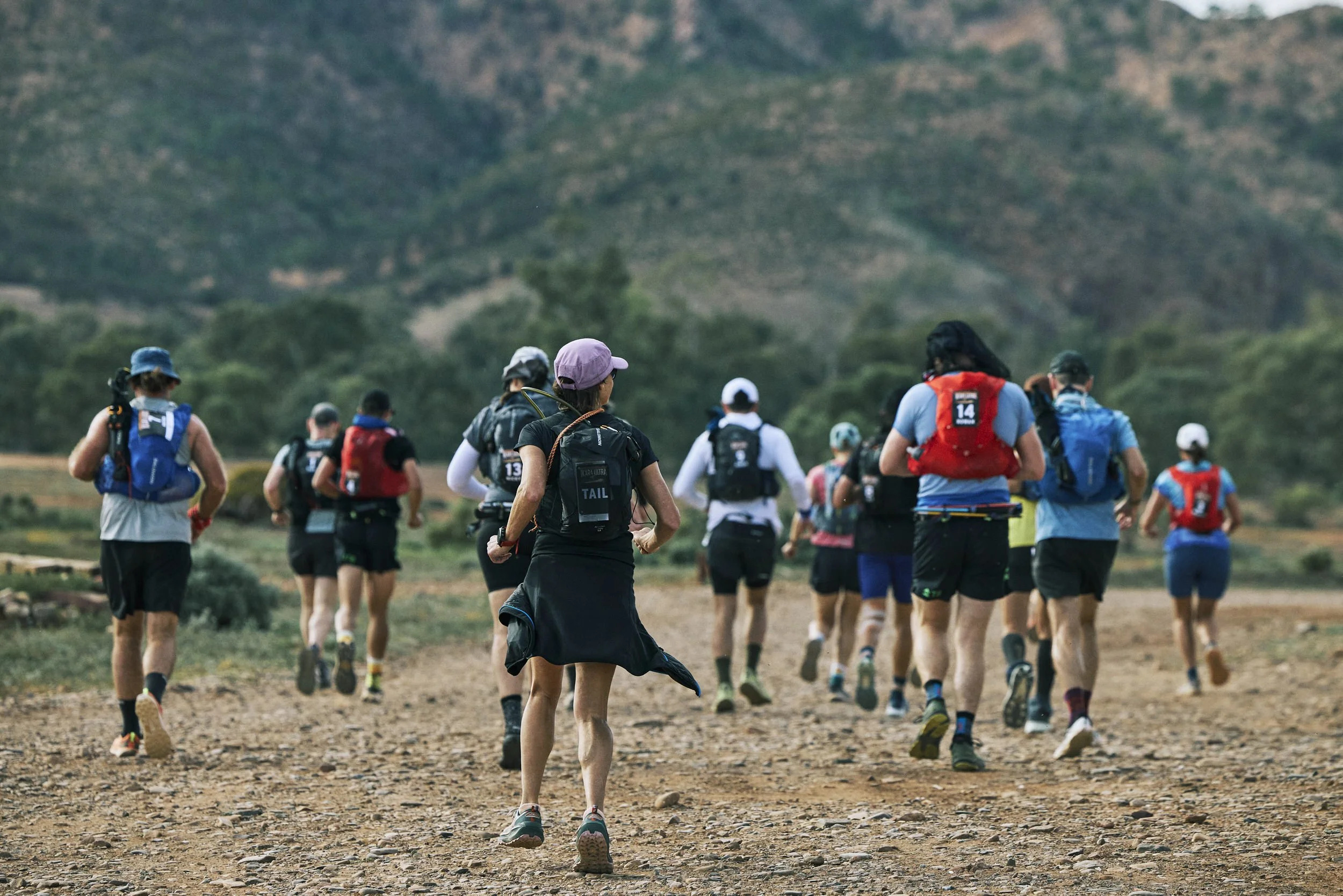 Group of people participating in an outdoor running event on a trail with mountains in the background.