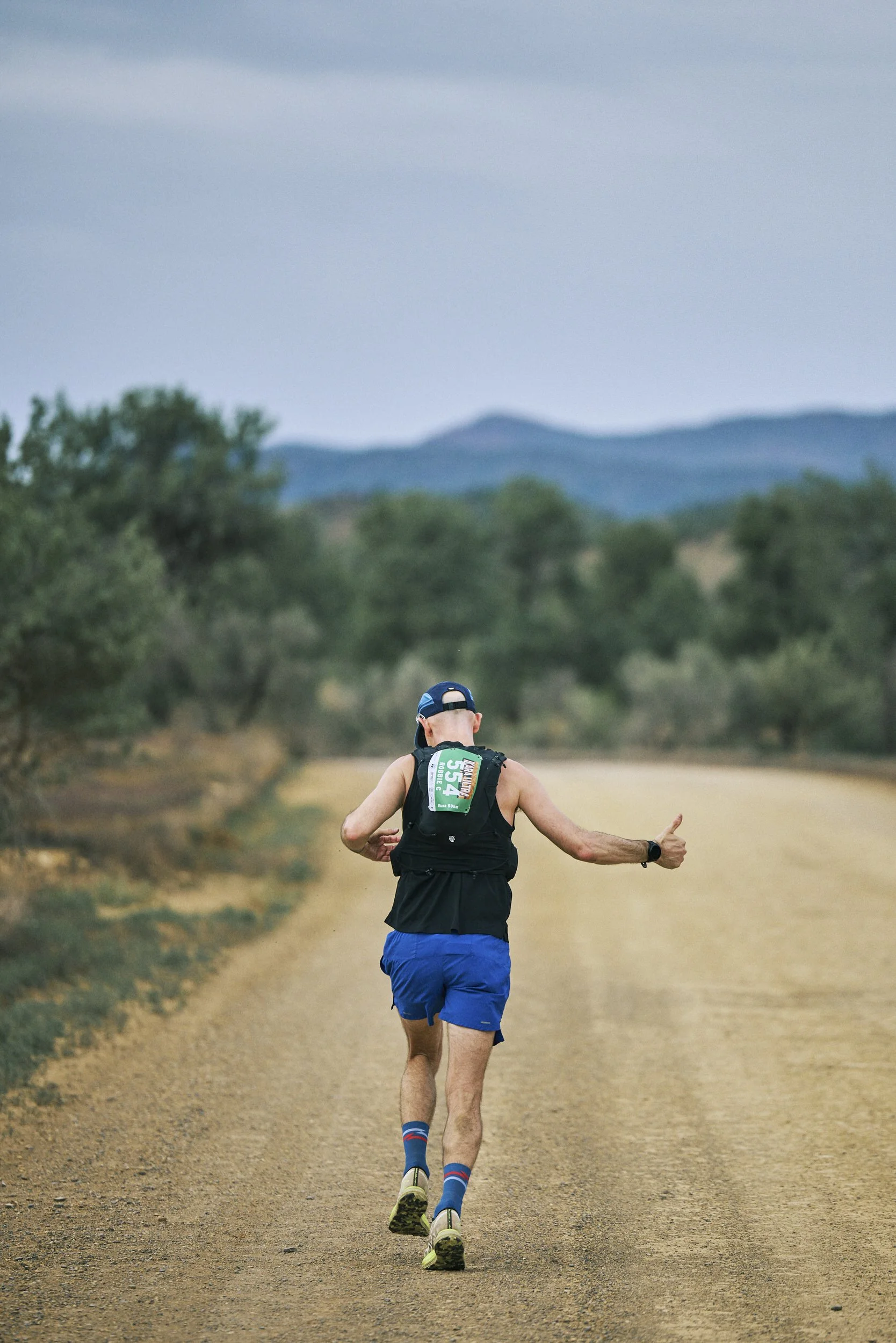 Women trail running in a forest with backpacks and walking poles, smiling, with a canopy and tents in the background.
